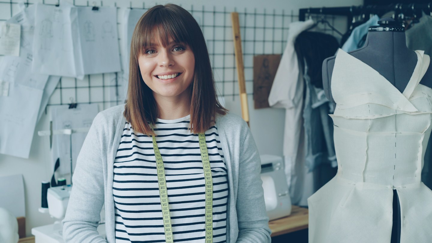 Diseñadora de moda sonriendo en su taller de costura creativo.